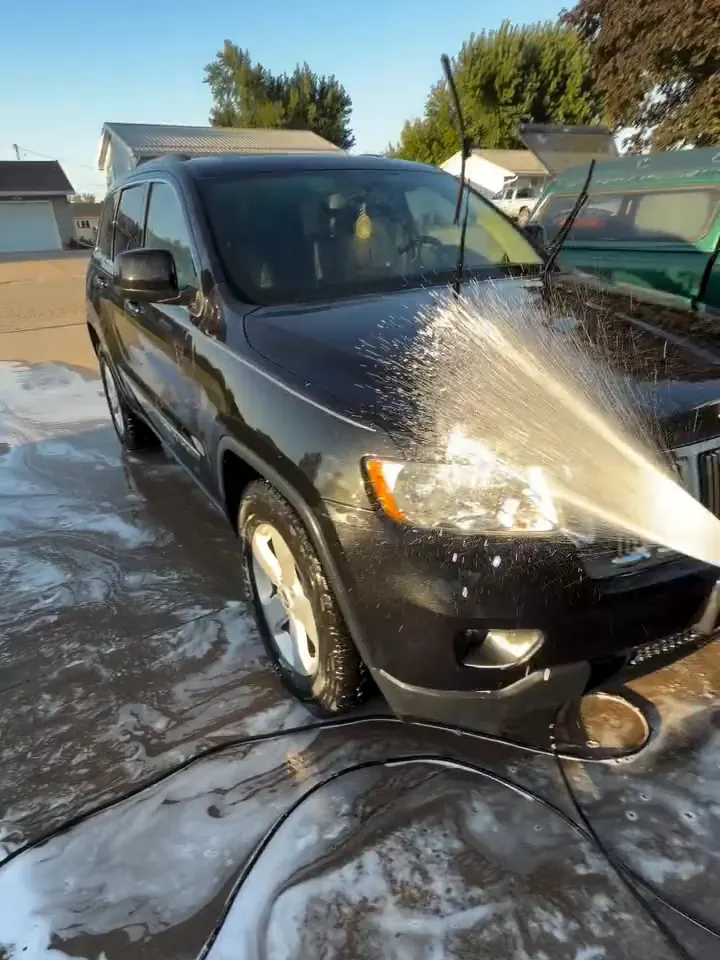 Foam prewash being rinsed off a black Jeep in a driveway