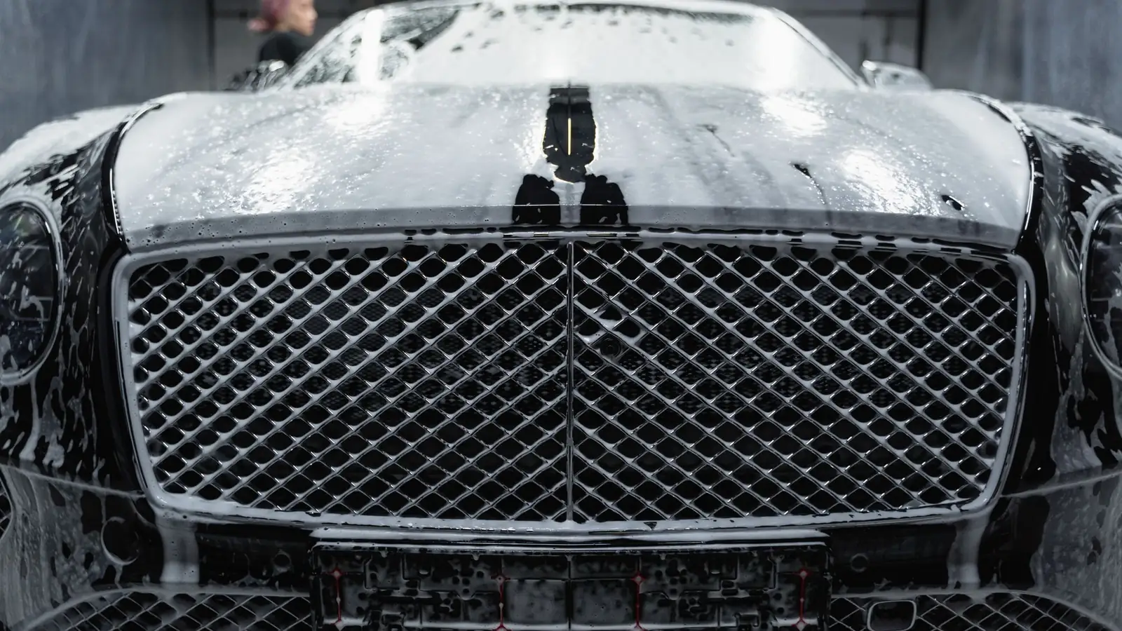 Front of a black car covered in wash foam